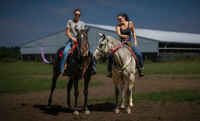 Haley and Mia on horseback beside a barn.