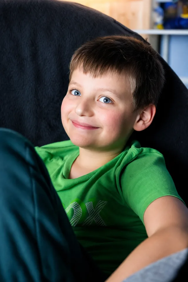 A relaxed portrait of a family member in a green shirt, seated against a dark chair.