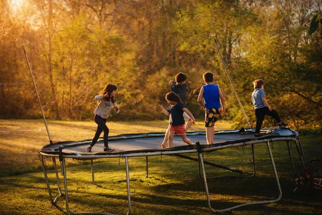 A candid family group playing on a trampoline in warm outdoor light.
