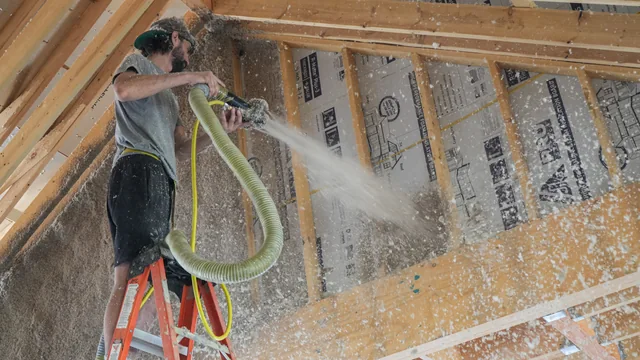 An Advanced Thermal Concepts technician on a ladder applying insulation inside a timber-framed room.